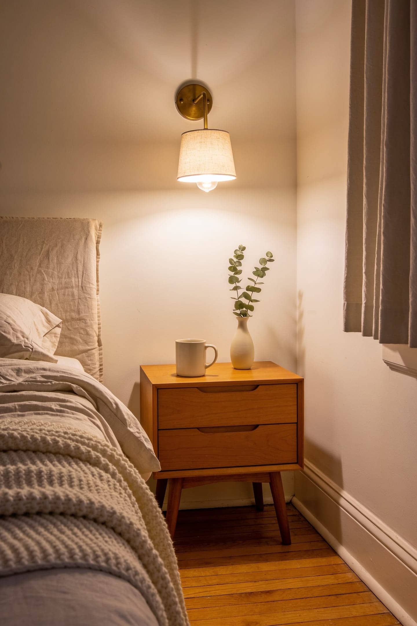 pair of cordless fabric shade wall sconces glowing warm on either side of a bed in a rental bedroom